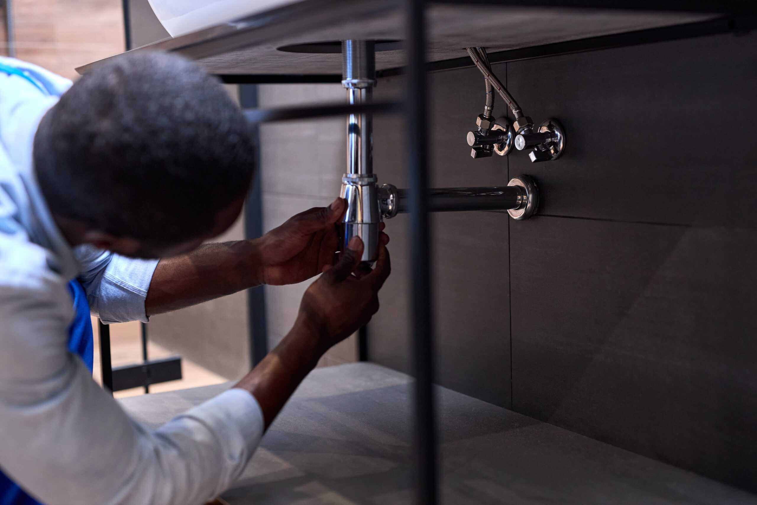 Handsome Hardworking Plumber Installing The Sink In Bathroom Close-up Photo, Cropped Black Man. Guy Is Repairing, Fixing Sink. Skilled Handyman During Work. Side View
