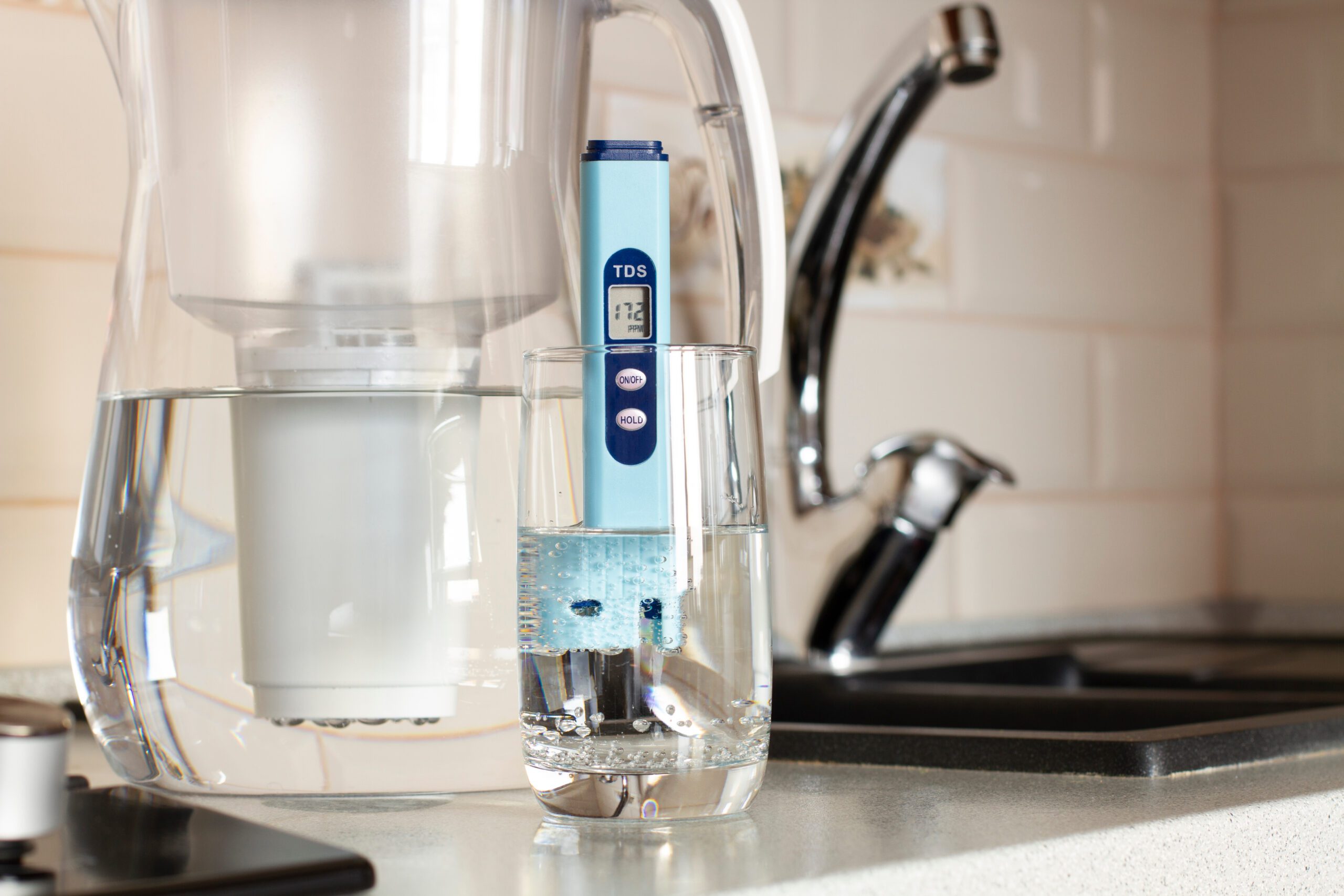 Measurement of TDS of water. Electronic pH meter in a glass of water.Filter for water purification. There is a tap for drinking water in the background.